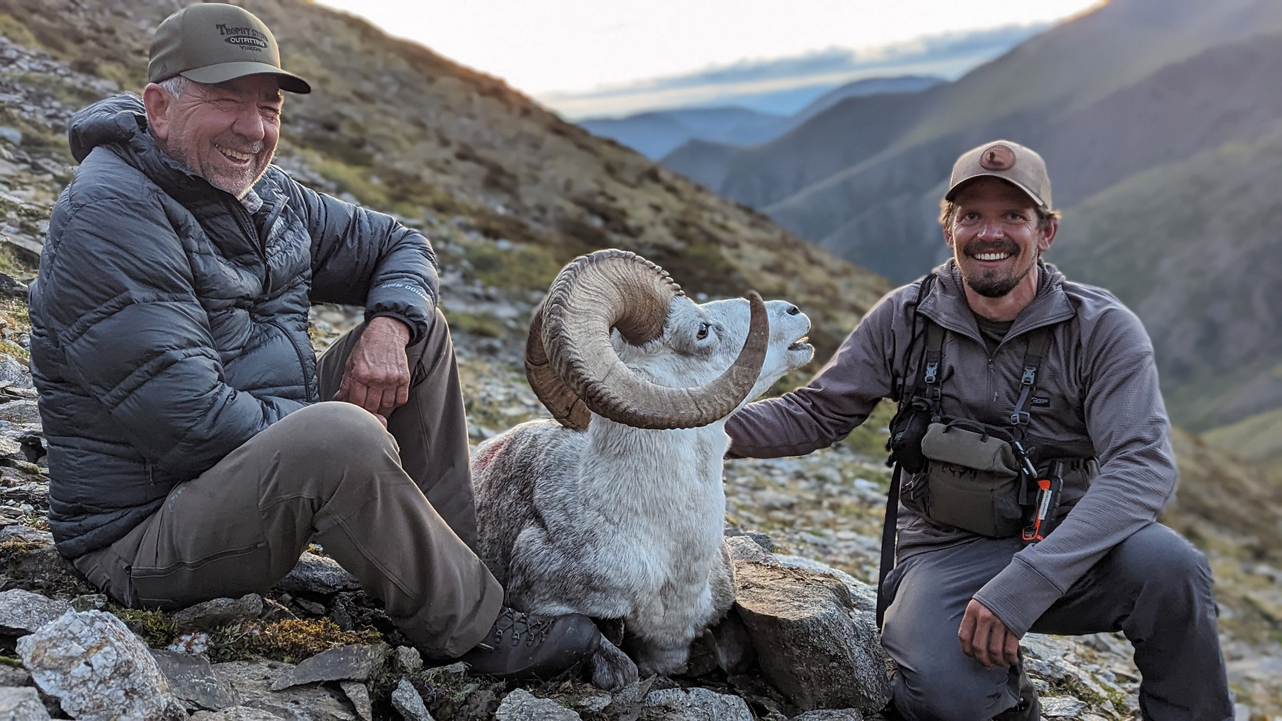 Big game hunter and guide with a ram in soft evening light